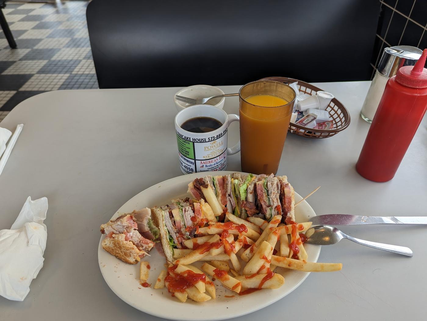 A club sandwich with fries, coffee and orange juice in a booth